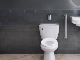 Restroom with a dark tile background and a tank toilet featuring a touchless flushing system