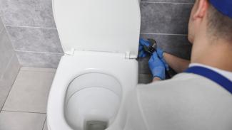 Plumber with a wrench fixing a toilet.