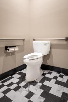 Pressure-assisted toilet in a beige bathroom with black and white tile floor